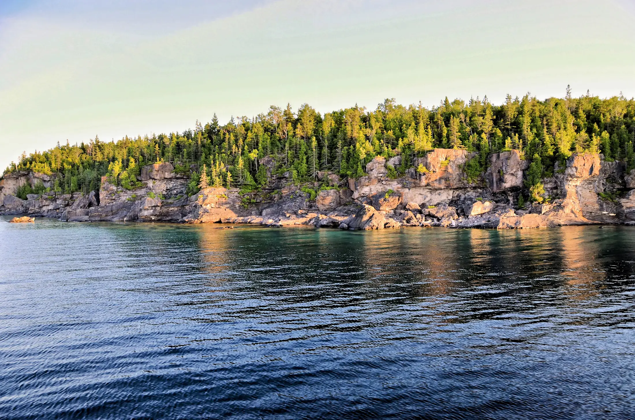 Limestone cliffs and pines above clear lake water in Canada at evening